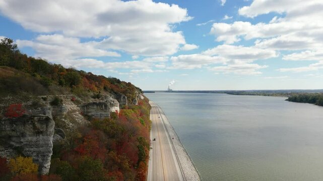 Rising drone shot of the Mississippi River Bluffs along the Great River Road in Illinois. The trees are displaying their autumn colors under a sunny blue sky.