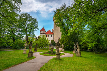 Scenic view of the Konopiste castle with its round tower and red roof. Surrounded by a lush green park adorned with classical statues and a winding pathway. Located near Benesov in the Czech Republic