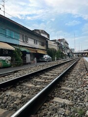 Obraz premium Platform and railway tracks through the city center with wooden houses on the side and a sky with white clouds.