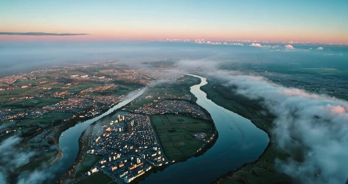 Aerial perspective from an aircraft window at a high elevation of a city enveloped in a layer of light misty smog and distant clouds during the evening.
