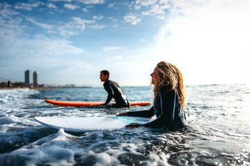 Fit couple surfing at sunset. Surfers friends having fun inside ocean. Sport and vacation concept