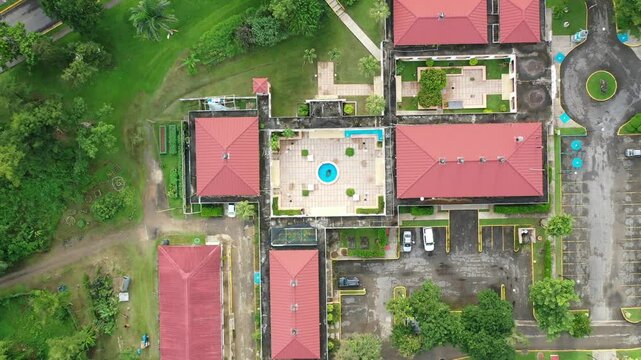 Drone top-down view of buildings with brown tiled roofs surrounded by greenery