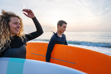 Young beautiful couple of friends on the sea with surfboards in their hands, sports active lifestyle