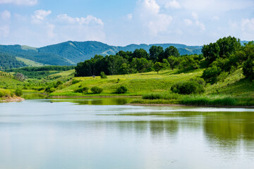 Beautiful Grassland Landscape with Lake and Mountains Wide grassland scenery with clear lake and distant mountains under blue sky. Peaceful natural landscape full of fresh green colors.