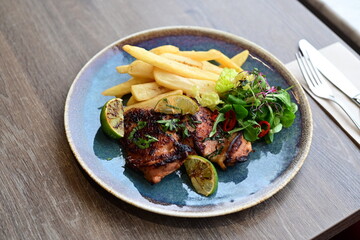 A plated serving of grilled Jamaican jerk chicken steak with crispy French fries and a fresh salad