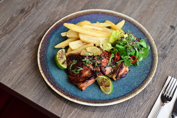 A plated serving of grilled Jamaican jerk chicken steak with crispy French fries and a fresh salad