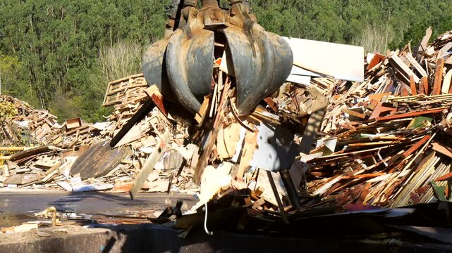 Industrial claw crane efficiently sorts and moves large piles of wood scraps at a recycling plant, promoting sustainable waste management