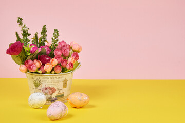 Pink roses in a bucket, Easter eggs next to them on a yellow and pink background