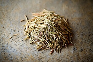 Fototapeta premium A close-up shot of a pile of dried rosemary leaves on a textured gray surface, highlighting their color and texture, perfect for culinary designs and presentations.