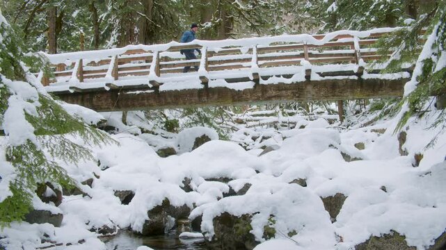 Fun in Snowy Forest with Man Crossing Wood Bridge Over Rocky Stream