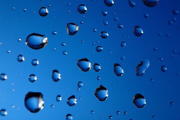 Bright and glossy blue water drops scattered across a smooth surface, creating a refreshing and dynamic visual effect, perfect for backgrounds, designs, and creative projects.

