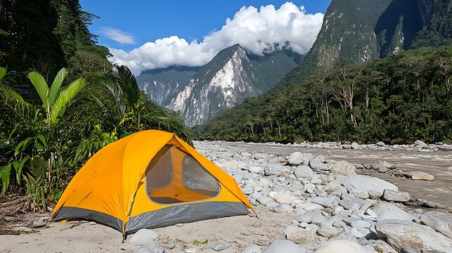 Orange tent pitched on rocky riverbank in lush mountain valley.