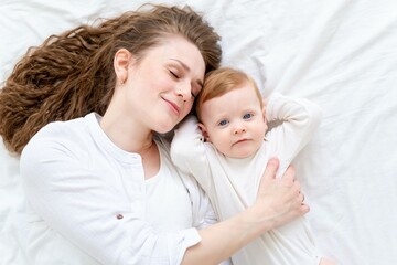 A loving mother takes care of her newborn baby son, gently hugging and kissing at home on a white bed background, maternal love and care. Portrait of a happy mother with a child, Lifestyle