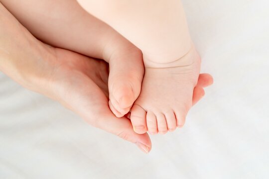 mom's hand holds the baby's little foot on the white background of the bed, mom's love and tenderness