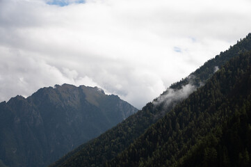 Beautiful view of a valley in the mountains on a summer day with thick clouds and rays breaking through. Close-up of the curve of the hills covered with forest