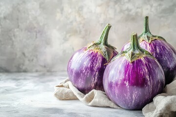 Fresh purple eggplants with green stems resting on a folded cloth