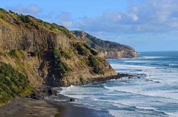 the dramatic cliffs and treacherous surf of muriwai beach on a sunny summer day near muriwai on the...