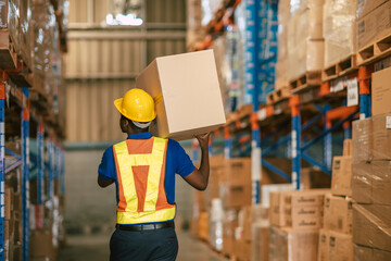 African black male warehouse worker carrying box in storehouse building with safety suit back view
