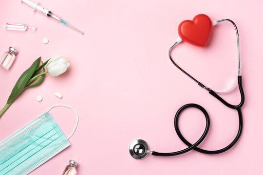Doctor's stethoscope with a red heart, white flower, syringe, ampoules and medical mask on a pink background. Copy space. Top view. - Powered by Adobe