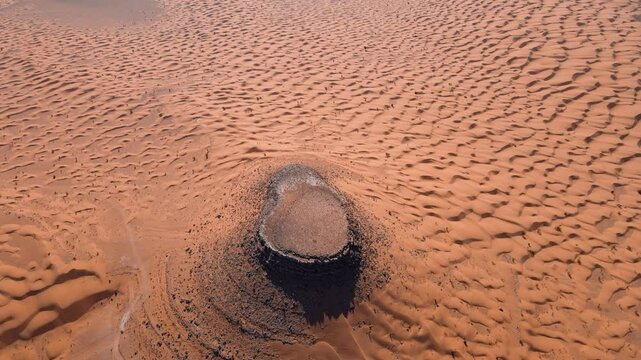 An intimate view of the Douz Tembaine desert, focusing on a prominent rock formation surrounded by intricate sand dune patterns, creating a sense of mystery and wonder.