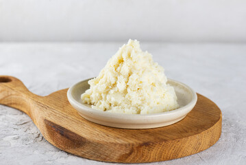 Shea butter in a plate on a wooden board on a light background.