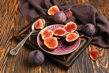 Plate with halves of fresh ripe figs on wooden background