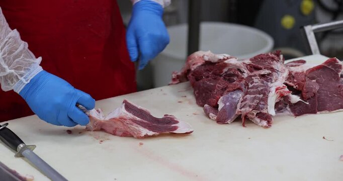 Meat industry, butcher cutting raw meat with knife at table in slaughterhouse.