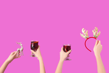 Female hands with glasses of warm mulled wine and Christmas decor on pink background