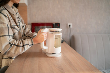 Woman Preparing to Boil Water Using an Electric Kettle in a Modern Kitchen While Enjoying a Sunny...