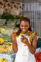 Successful African female small business owner excited, celebrates with joy looking at her smartphone at her local grocery store.