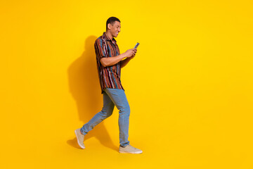 Young stylish man walking with phone against a bright yellow background expressing happiness and leisure