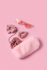 Cosmetic bag with sunglasses, bracelet and scrunchies on pink background