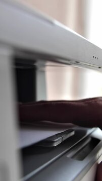 A girl office worker makes a photocopy of documents using a photocopier. The director's secretary is doing his job. Clerk in the office during work with copier. Vertical video.