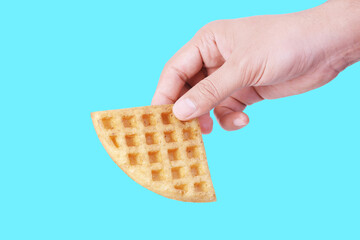 Hand Holding a Golden Waffle Slice on Vibrant Blue Background–Perfect for Food Advertisements and Social Media Promotions