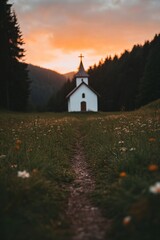 Fototapeta premium Serene white country church in meadow at sunset. Path through wildflowers leads to chapel. Scenic landscape for Christian worship, Easter, Christmas, or wedding photography