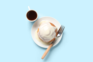 Plate with tasty glazed cinnamon bun, fork and cup of tea on blue background