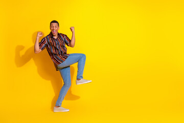 Joyful young man in colorful casual outfit posing on a vibrant yellow backdrop, expressing...