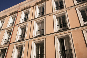 Facade of an apartment block building in old Spanish town. Yellow beige house wall with many windows, balconies with wooden shutters bottom view.