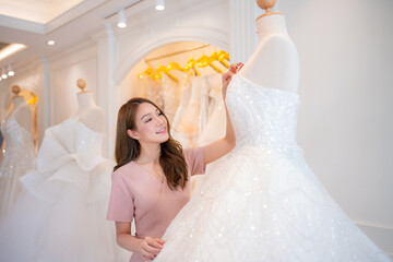 Attractive young bride is smiling while choosing wedding dress in modern wedding salon.