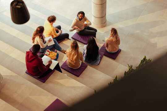 University teacher talking to students sitting on cushions in modern building