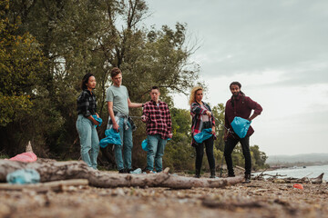 Volunteers cleaning plastic waste on river shore holding garbage bags
