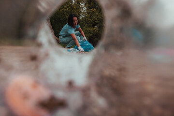 Shot from a plastic bottle perspective of female volunteer picking up trash
