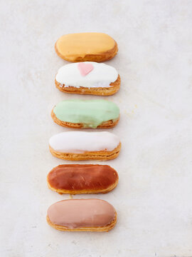 Delicate pastries with vibrant icing are beautifully arranged in a vertical line, showcasing an array of colors and flavors under the warm afternoon sun in a charming bakery setting