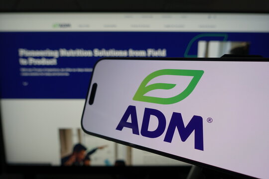 Kiel, SH, Germany March 24 2025: Smartphone displaying ADM logo in front of company website on a monitor, illustrating a digital business environment. The image captures a tech-savvy workspace