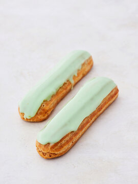 Soft, airy pastries topped with a glossy green glaze sit elegantly on a smooth surface, inviting dessert lovers to indulge in this delectable treat. These eclairs promise sweet joy