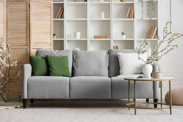 Grey sofa and vase with blooming branches on coffee table in interior of modern living room