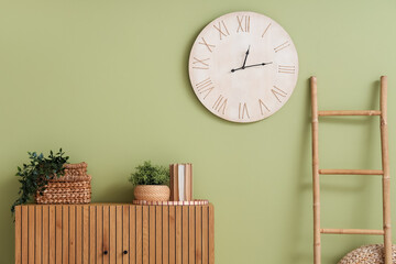 Chest of drawers, houseplants and clock on green wall in room