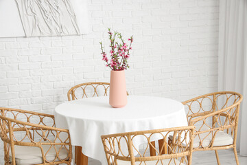 Vase with blooming Sakura branches on table near armchairs in dining room