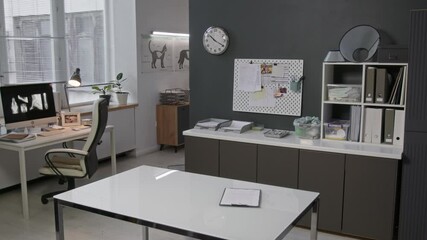Interior of modern veterinary office with computer displaying x-ray images on desk, shelves with medical supplies, bulletin board and clipboard with medical form on table