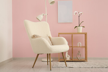 White armchair, lamp and shelving unit near pink wall